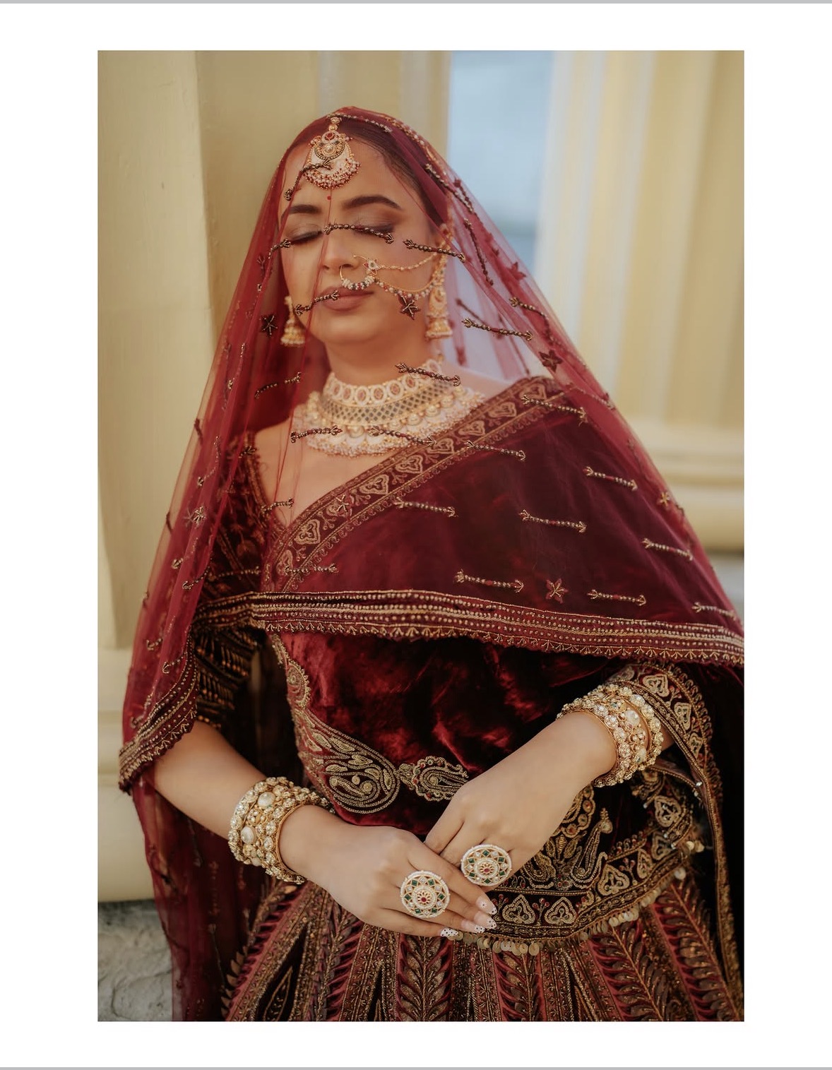 Bride behind a red sheer veil with heavy gold and pearl jewellery